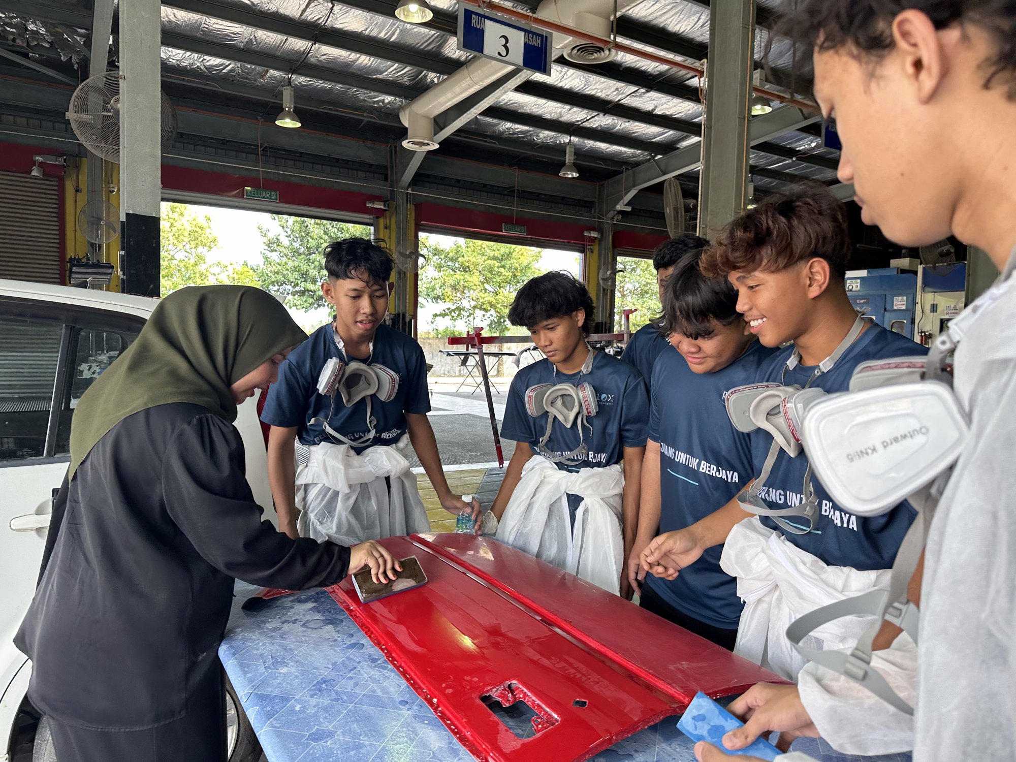Students practising spray painting on a red body panel under coach supervision