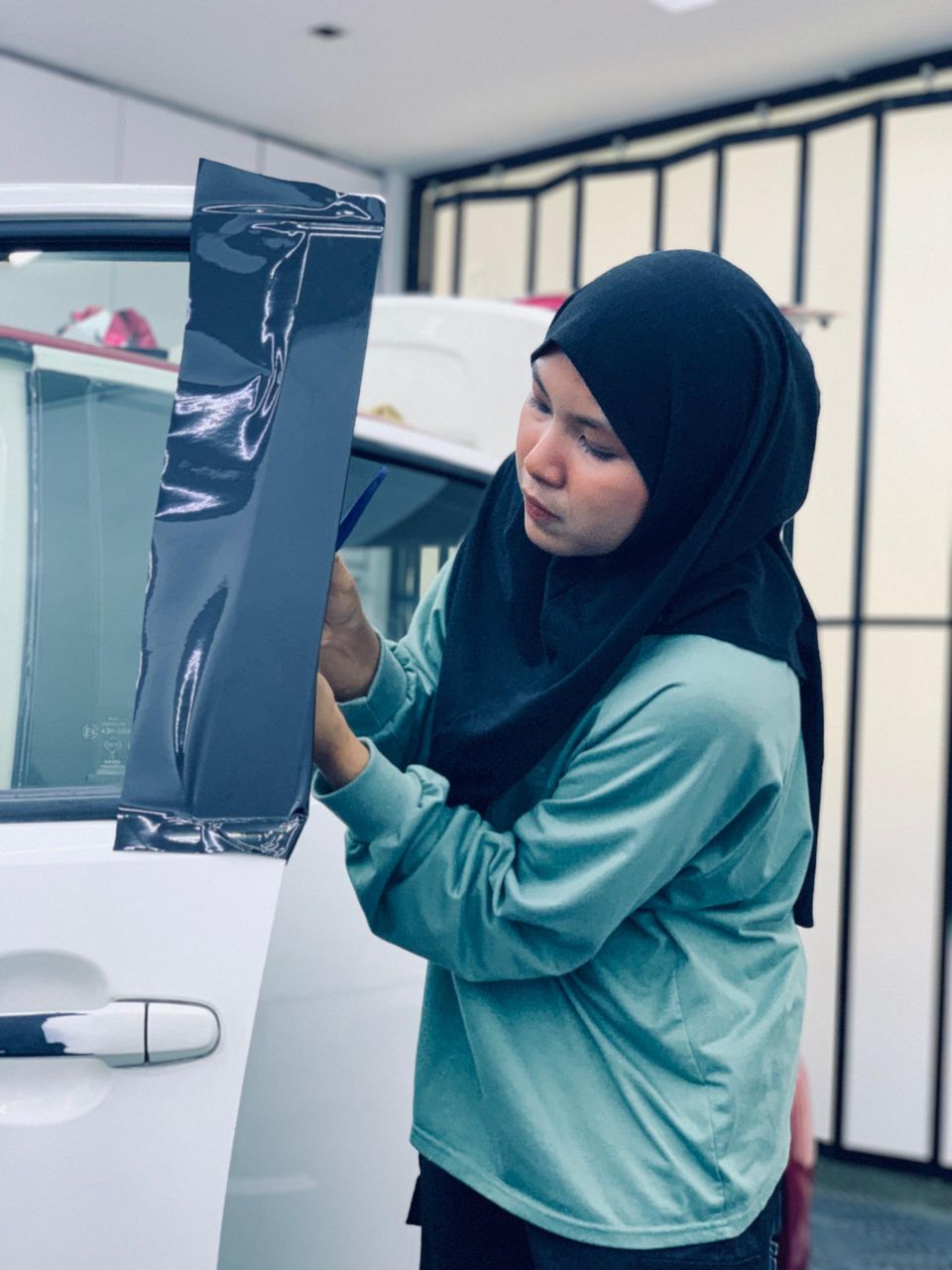 Pelajar wanita P10X Academy memasang vinyl wrap gelap pada pintu kereta